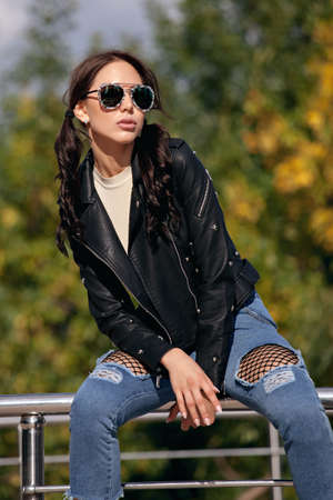 fashionable young woman in rock style clothes, black leather jacket, blue jeans, tights in a grid under battered jeans.の写真素材