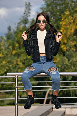 fashionable young woman in rock style clothes, black leather jacket, blue jeans, tights in a grid under battered jeans.の写真素材