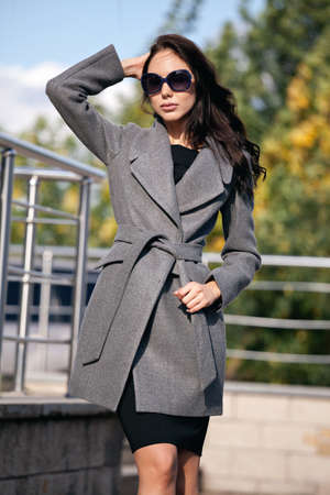 Outdoor portrait of a young beautiful fashionable woman, outdoors. A model dressed in a stylish gray coat, sunglasses. The concept of womens fashion, urban lifestyleの写真素材