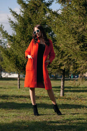 Outdoor portrait of a young beautiful fashionable woman, outdoors. The model, dressed in a stylish orange coat, sunglasses. The concept of women's fashion, urban lifestyle.の写真素材