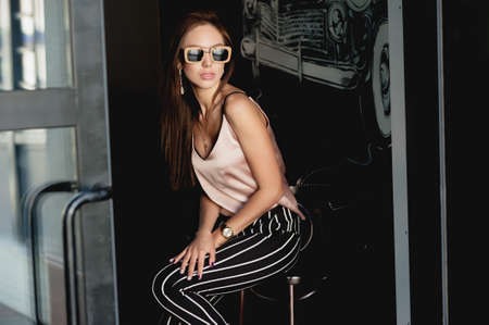 Young and beautiful girl in a beige t-shirt and black breeches in a white stripe. Women's fashion. Urban way of life.の写真素材