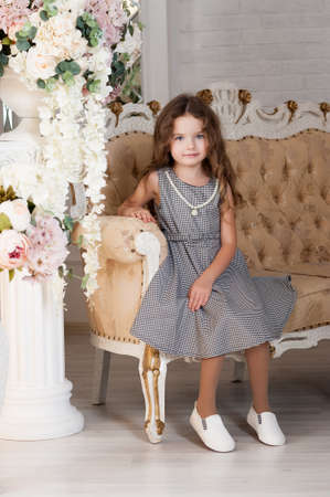 A little girl of seven years with brown hair, sitting next to a bouquet of peony flowers, smiling, in a gray dress in a cage, curls. The concept of a holiday.の写真素材