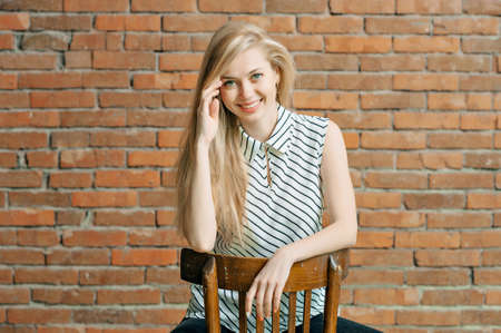 A blonde girl is calling by the phone against a brick wall background, calling the apartment repair service. Advertising of construction servicesの写真素材