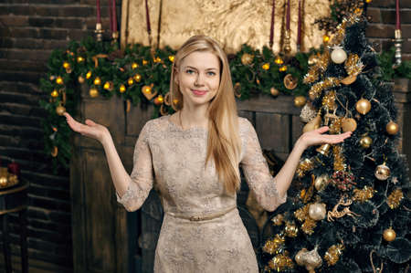 Young woman in a cozy interior of Christmas. The girl sits under a Christmas tree among many gifts. Preparing for Christmas. The concept of a holidayの写真素材