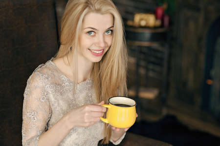 Young woman in a cozy interior of Christmas. A girl is sitting with a yellow mug under a Christmas tree among many presents. Preparing for Christmas. The concept of a holidayの写真素材