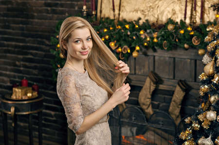 Young woman in a cozy interior of Christmas. The girl sits under a Christmas tree among many gifts. Preparing for Christmas. The concept of a holidayの写真素材