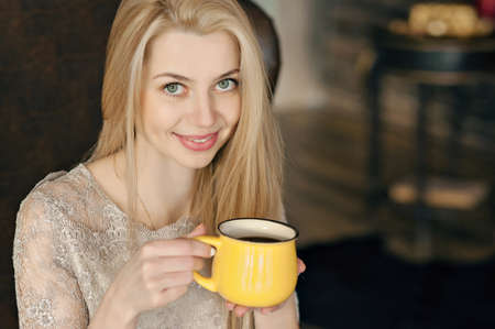 Young woman in a cozy interior of Christmas. A girl is sitting with a yellow mug under a Christmas tree among many presents. Preparing for Christmas. The concept of a holidayの写真素材