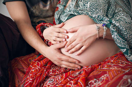 Cropped image of a beautiful pregnant woman and her beautiful husband hugging her tummy. Dressed in traditional Indian outfit shalwar kamizの写真素材