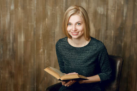 Young blond woman at home, reading book. Wooden wall loft backgroundの写真素材