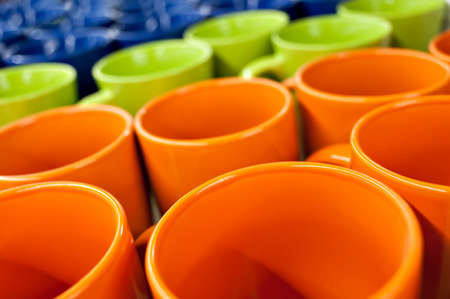 Ceramic Mugs and bowls of different colors in the store on the counter, stand in a row pile. Sale, trade.の写真素材