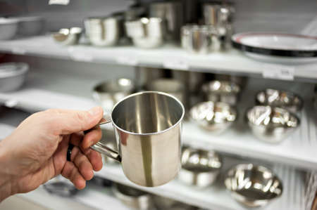 The buyer's hand of a man with a steel bowl on the background of a rack with utensils made of steel.の写真素材