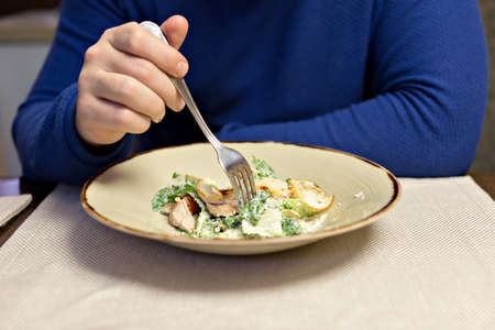 A man in a blue sweatshirt with a fork in his hand eating a salad. Close-up.の写真素材