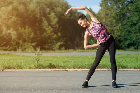 Beautiful young woman, brunette, doing warm-up before jogging in the park, wearing headphones, listening to music.の写真素材