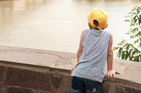 The boy is 5 years old, stands with his back and looks at the riverの写真素材