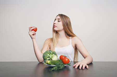 Beautiful young girl at a table with vegetables for salad. Cook at home. Concept of healthy, vegetarian foodの写真素材