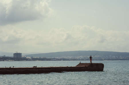 Fisherman with a fishing rod on a sea pier in the background of the city.の写真素材