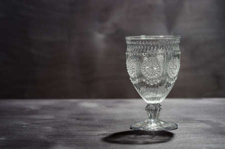 empty crystal glass with a pattern and shadow from it, on a dark wooden background.の写真素材