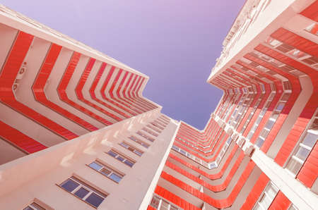 View of a residential building from the bottom up. White house with red balconies in a warm sunny dayの写真素材