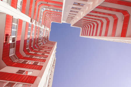View of a residential building from the bottom up. White house with red balconies in a warm sunny dayの写真素材