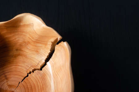 Detail of a simple brown wooden bowl with a crack on the edge on a black wooden background and copy spaceの写真素材