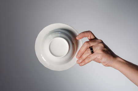 Male hand holding a white plate, on a light background. bottom viewの写真素材
