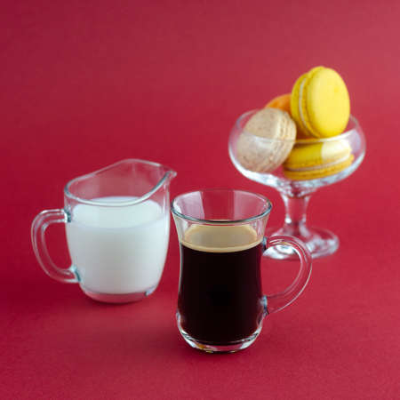A transparent cup of black coffee and a milkman and a vase with cookies placed on a red surfaceの写真素材
