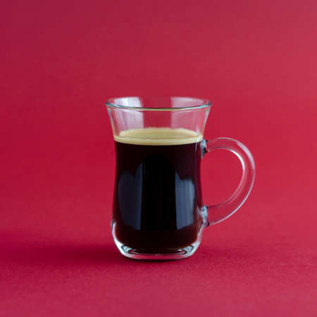 Transparent cup of black coffee placed on a red surface.の写真素材