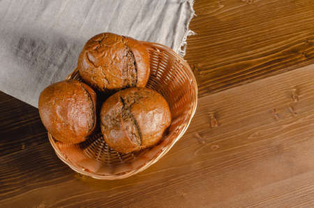 Craft three bread buns in a wicker basket, on a wooden cutting board. Simple breakfast on wooden background. copy space.の写真素材