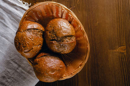 Craft three bread buns in a wicker basket, on a wooden cutting board. Simple breakfast on wooden background. copy space.の写真素材