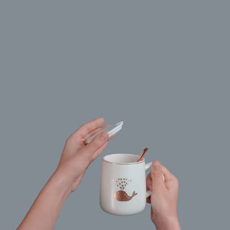 White cup with a spoon in the hand of a teenager, on an isolated gray backgroundの写真素材