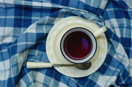 Top view: a cup of coffee, tea on a saucer and a teaspoon on a checkered napkin in blue and white. copyspace.の写真素材