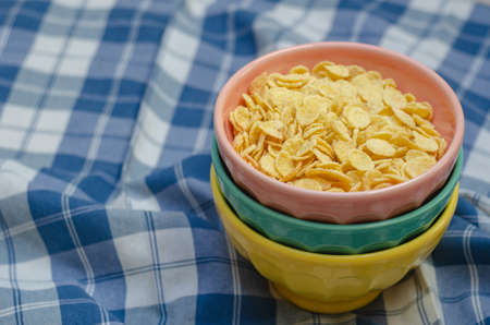 Cornflakes and three bowls of different colors, on a plaid napkin in blue and white. copy space.の写真素材