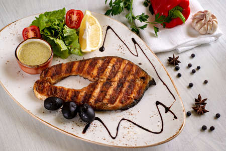 Grilled salmon steak, served with sauce, lemon, lettuce and tomatoes, on a white dish. Copyspace.の写真素材