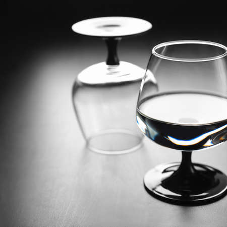 Two glasses on a black leg, one with water, the second turned upside down, against a dark background. Copyspaceの写真素材