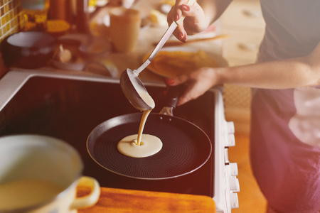Cooking pancakes. In kitchen on a round skillet liquid dough from the ladle is pouredの写真素材
