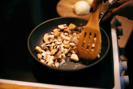 A woman is frying mushrooms and carrots in the kitchen. The process of frying in a frying pan. Preparation of food by prescription. Home kitchen. Mom cooks fried mushrooms and carrots.の写真素材