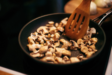 A woman is frying mushrooms and carrots in the kitchen. The process of frying in a frying pan. Preparation of food by prescription. Home kitchen. Mom cooks fried mushrooms and carrots.の写真素材