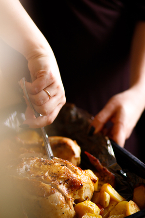 The womancooked chicken and fried potatoes. Submission of the finished dishes. Cutting fried chicken. Festive dish cooking.の写真素材