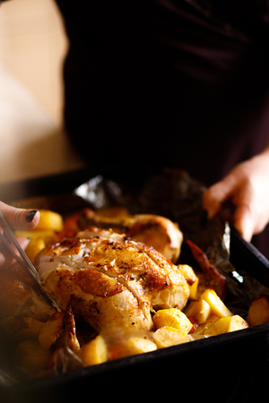 The womancooked chicken and fried potatoes. Submission of the finished dishes. Cutting fried chicken. Festive dish cooking.の写真素材