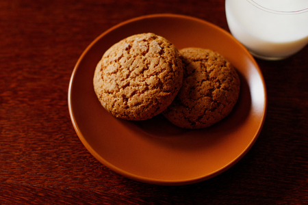 A glass of fresh homemade milk and delicious oatmeal cookies on a wooden table. Mom cooked a healthy breakfast.の写真素材