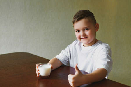 Son drinks milk in the kitchen in the morning. A young boy shows a class, a glass of tasty, homemade milk. Healthy breakfast.の写真素材