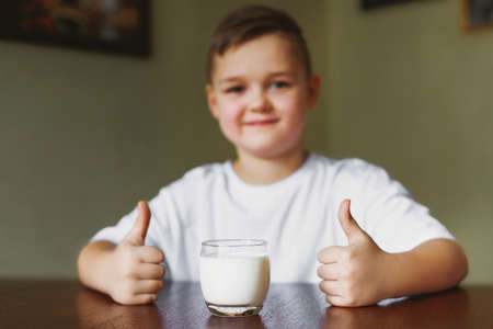 Son drinks milk in the kitchen in the morning. A young boy shows a class, a glass of tasty, homemade...