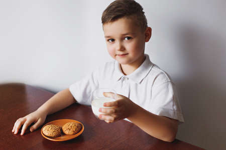 A little boy eats oatmeal cookies and drinks with home-made milk. Healthy breakfast prepared by my mother. The schoolboy is having breakfast.の写真素材