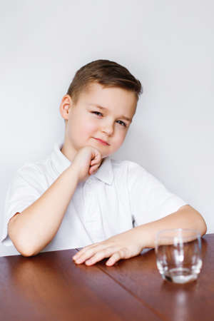 A young boy is sitting at a table in the kitchen with an empty glass.の写真素材