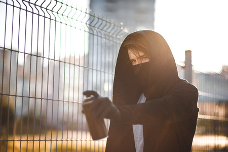 Man with mask and gloves is holding a spray can with paint. Street vandalism, urban style. Graffiti drawings. Aerosol in hand.の写真素材