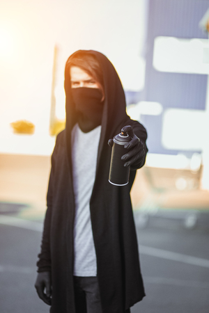 Man with mask and gloves is holding a spray can with paint. Street vandalism, urban style. Graffiti drawings. Aerosol in hand.の写真素材
