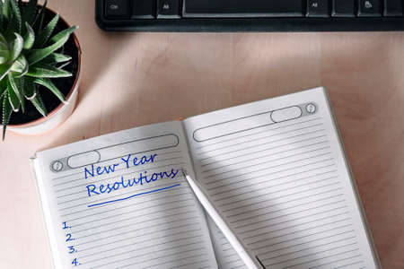notepad entry: "New Year's resolutions." Notebook lies on a wooden table. top black keyboard, cactus on the left.の写真素材
