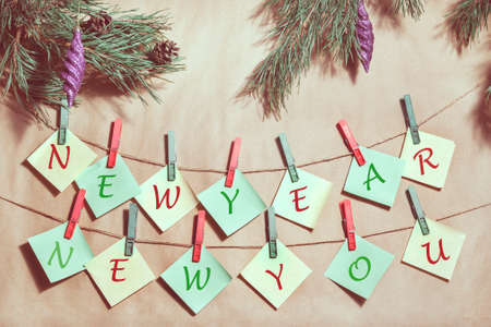 on a paper background hang yellow and green stickers attached to the rope with red and green clothespins. on top of a pine branch with cones. on each sticker by letter, I add up to the inscription:の写真素材