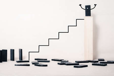 On a light background a wooden box. At the top of the box is a domino. Below are the fallen dominoes. a ladder leads to the box with a queue of dominoes.の写真素材