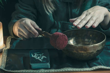 witch plays on a tibetan bowl. on the right is a deck of tarot cards.